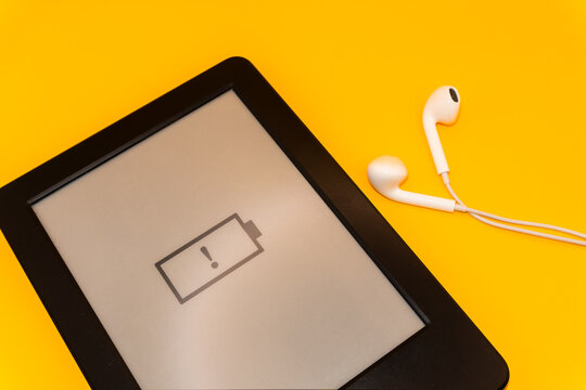Concept audiobook with headphones A dead battery on a modern device on a yellow background, a device without a charger, a dead phone, a dead battery on an e-reader, copy space High quality