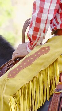 Cowboy with yellow chaps sitting in saddle long shot