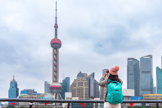 Young woman and a backpack takes a photo of the shanghai skyline, from the bund view point. a famous travel destination for solo female travelers in asia.