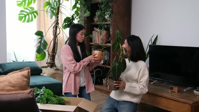 Smiling female friends unboxing and decorating their living room with new green potted plants