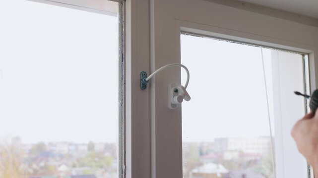 Static shot of a man installing a child safety window lock with a power drill