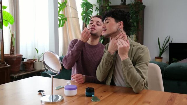 Two young men are sitting at a table applying cosmetic products during their daily beauty ritual