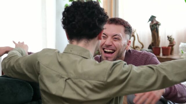 Two young men in love talking intimately before sharing a joyful hug on a sofa at home