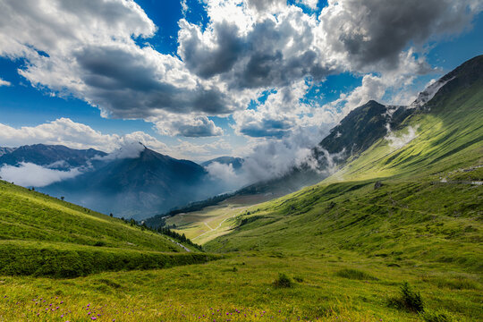 A lush green alpine meadows under a cloudy sky at the Colle delle Finestre mountain pass in Piedmont, Italy.