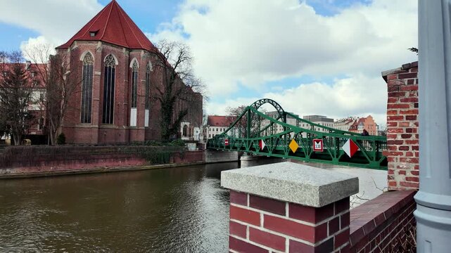 Scenic Tumski Bridge over the Odra River in Wroclaw, Poland, historic red brick Gothic cathedral in background, beautiful sunny day, popular travel destination, city landmark, urban photography.