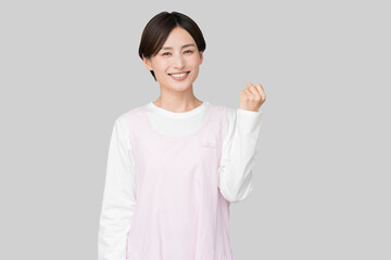 笑顔でガッツポーズをするエプロン姿の女性（保育士・介護士・家事代行イメージ） © lielos