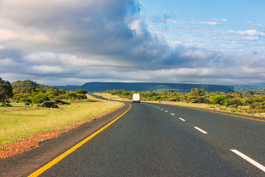 Paved Two-Lane Highway Winding Through Vast Green Savanna Landscape van driving toward distant hills.