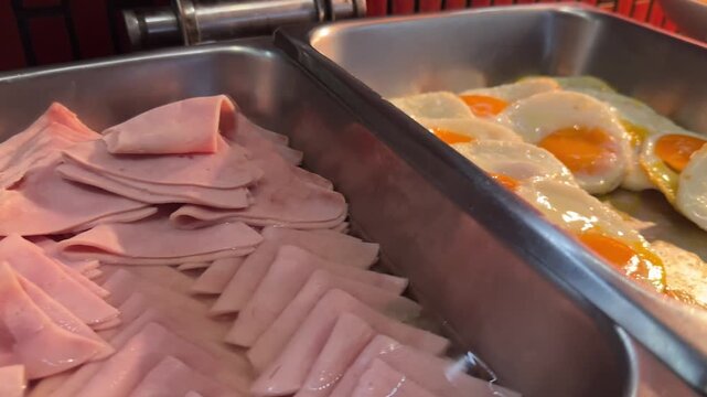 Video of breakfast buffet with fried eggs and sliced ham in stainless chafing dishes hot food display