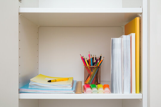 Different school accessories on white wardrobe shelf. Closeup. Front view.