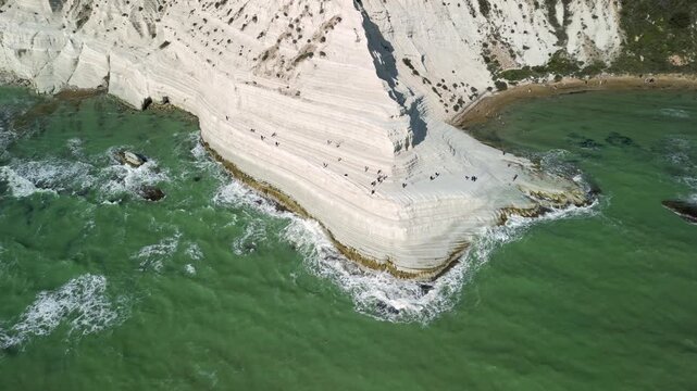 Aerial view of white limestone cliffs with visitors walking along the edge, turquoise waves crashing against the shore, showcasing the stunning natural landscape of the coast