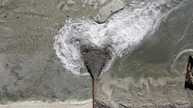 Aerial drone close-up of dredging pipe discharging sand for beach nourishment.