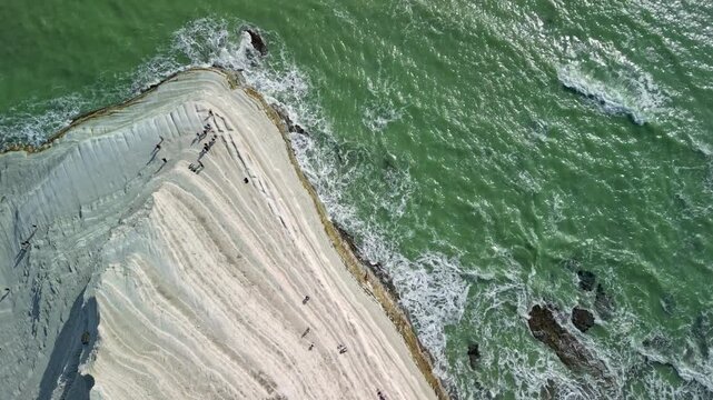 Aerial view of a coastal cliff with layered white rock formations and turquoise waves crashing against the shore, showcasing the natural beauty of the landscape