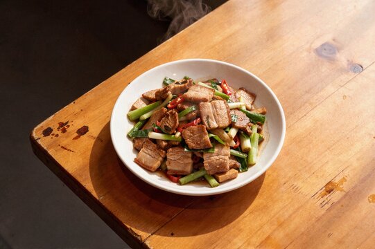 Stir fried pork belly with green leeks and chili on wooden table for authentic Chinese Sichuan cuisine menu and restaurant marketing