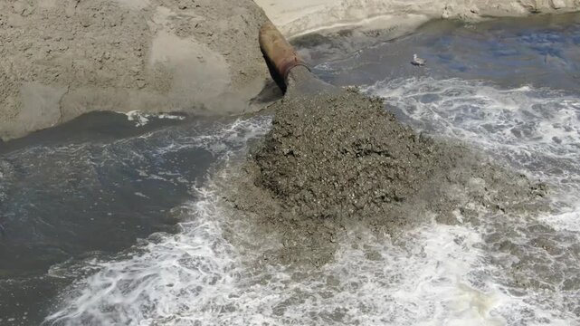 Aerial drone close-up of dredging pipe discharging sand for beach nourishment.