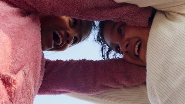 Two young Indian girls create a playful frame with their hands while looking down at the camera, capturing a joyful and interactive childhood moment in a simple rural setting