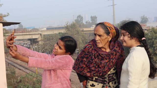 Happy Indian village moment as two young girls take a selfie with their grandmother, capturing joy, bonding, and modern technology blending with traditional rural life in Uttarakhand mountains.