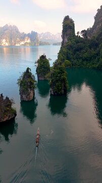 Discover the stunning landscapes of Khao Sok National Park in Thailand. A traditional longtail boat glides through serene waters, surrounded by lush greenery and towering limestone formations.