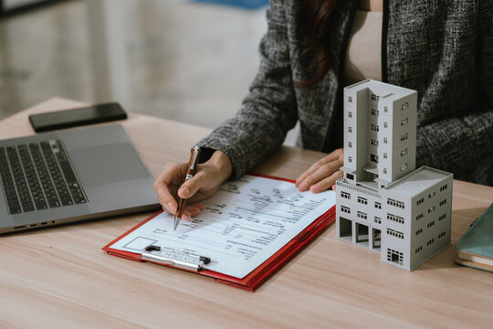 Businesswoman holding a small building model at a desk with a laptop and documents, representing real estate investment, property management, and financial decision-making.