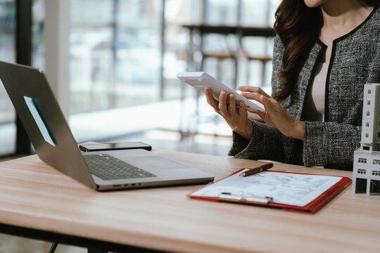 Businesswoman holding a small building model at a desk with a laptop and documents, representing real estate investment, property management, and financial decision-making.