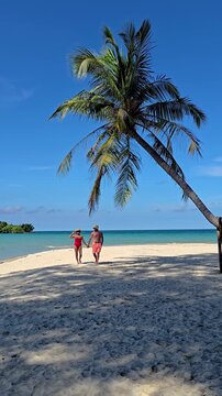 Two people stroll on a pristine Koh Kood Island beach, surrounded by clear turquoise waters, swaying palm trees, savoring the perfect tropical vibe, A couple of men and women on vacation in Thailand
