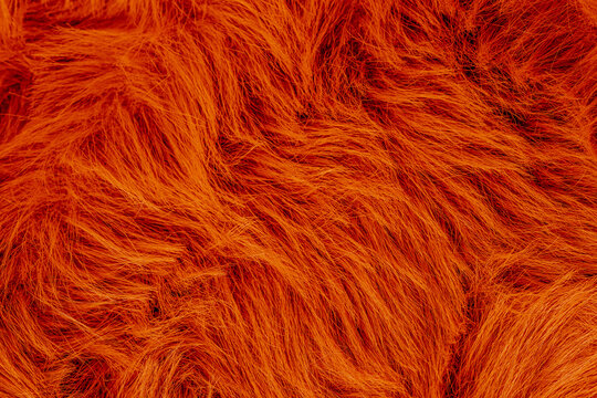 Close up of vibrant orange artificial fur texture background with long soft shaggy fibers surface