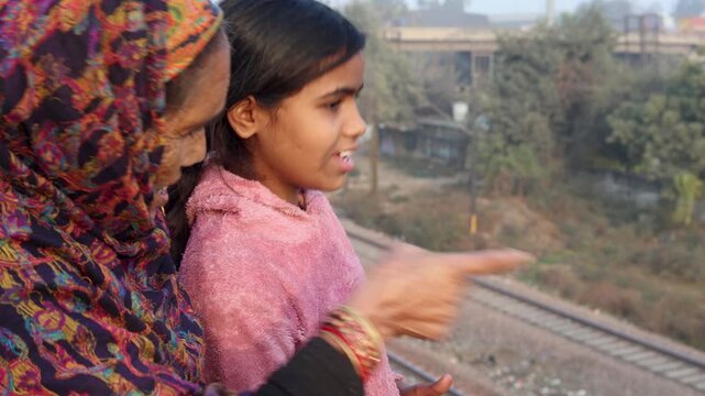 A young girl pointing into the distance while standing beside an elderly woman, capturing a moment of curiosity, guidance, and intergenerational connection in a simple outdoor setting.