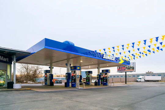 Rome, NY - Apr 6, 2026: A wide view of the Sunoco gas station is captured at dusk in Rome, NY, featuring blue and yellow pennant flags. Sunoco, founded in 1886, operates over 5,200 retail locations