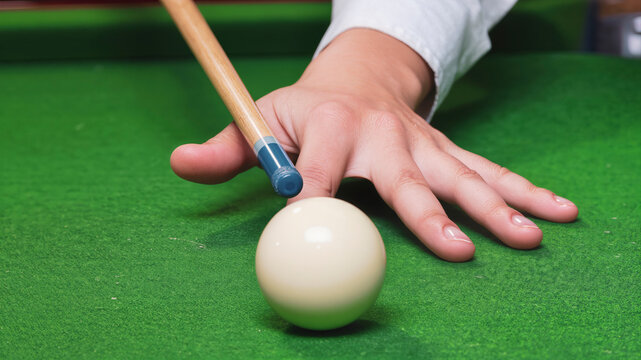 Close up of hand aiming cue at white billiard ball on green table, preparing precise shot in pool game. Leisure activity and skill practice in recreational environment