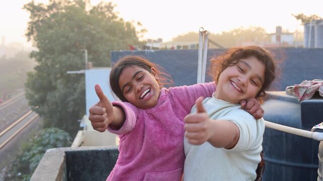 Two happy young girls standing outdoors, smiling brightly and giving thumbs up, capturing a joyful friendship moment with warmth, positivity, and carefree childhood energy in a natural setting.