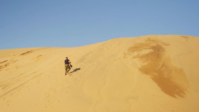 Caucasian Couple Climbing And Sandboarding Down Steep Golden Dune, Boards And Footprints Trace Slope, Bright Sky And Warm Sand Create Active Travel Journey Scene Of Recreation And Teamwork