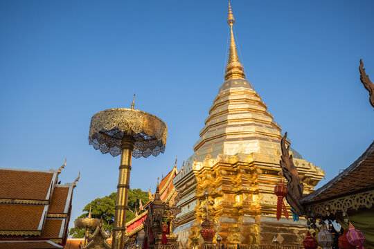 Gleaming golden stupa and ornate ceremonial umbrella under a clear sky at the sacred Wat Phra That Doi Suthep, Chiang Mai, Thailand.