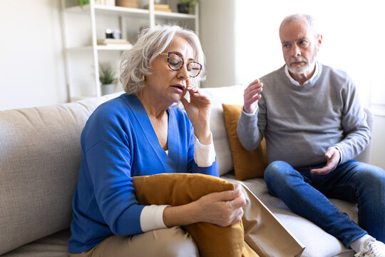 Senior couple arguing on sofa at home: frustrated woman listening to man complaining
