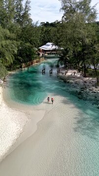 Two travelers stroll along the soft sandy shore of Koh Kood Island Thailand. The clear turquoise waters reflect the surrounding lush greenery, creating a picturesque tropical paradise.