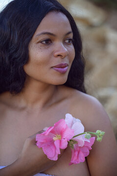 Profile portrait of a young Black woman holding pink mallow flowers