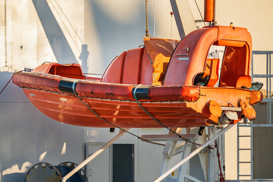Orange emergency rescue boat or fast rescue craft mounted on a ship deck davit system under warm sunset light