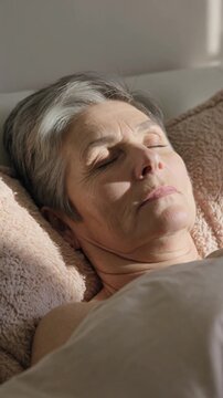 Senior woman sleeping peacefully in bed with morning sunlight, vertical shot