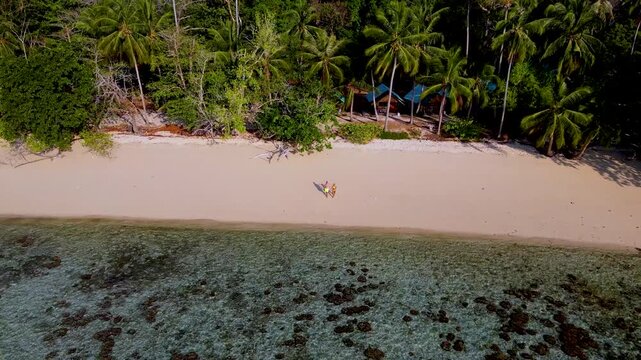 a couple on vacation on the beach in Thailand, A turqouse colored ocean with clear water at Koh Kradan, a tropical island in Trang, Thailand, and a coral reef in front of a tropical island