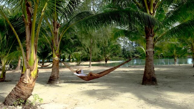 An Asian woman enjoying serene moments in a hammock surrounded by lush palm trees on Koh Kood Island, Thailand. This tranquil location offers a perfect escape for relaxation and rejuvenation.