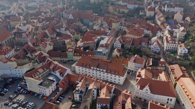 Bird's-eye view of the medieval old town of Meissen. The image shows the dense network of red tiled roofs, historical buildings, and winding alleys in warm daylight.