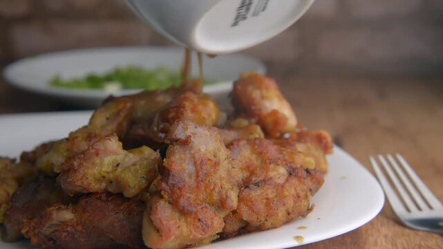 Breaded chicken seasoned with salt and pepper, bathed in a spicy sauce of mushrooms, onions and spices, on a white plate with a fork beside it on a rustic wooden table with a brick wall in the backgro