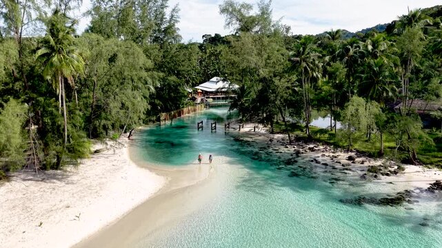 Explore the serene beaches and crystal-clear waters of Koh Kood Island in Thailand. Palm trees sway gently while two travelers stroll along the shoreline, enjoying the natural beauty and tranquility.