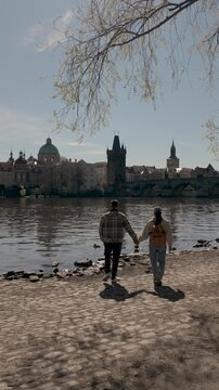 Two friends enjoy a beautiful day by the riverside in Prague, capturing the stunning cityscape and the gentle lapping of the water. A perfect setting for relaxation and connection.