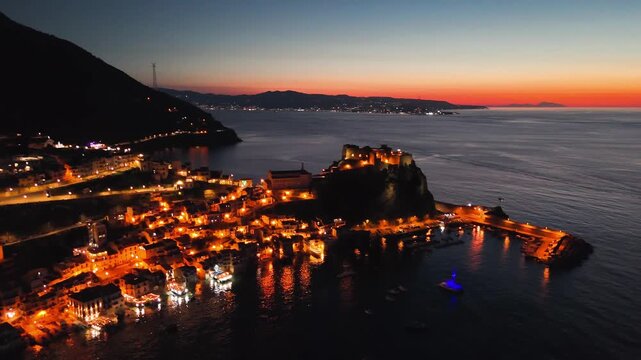 Breathtaking aerial view of Scilla at night from Chianalea, showcasing the iconic Ruffo Castle dramatically illuminated on its rocky promontory