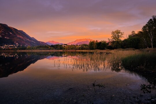 Vibrant sunset colors reflecting on Lake Pusiano with silhouettes of trees, Lombardy, Italy
