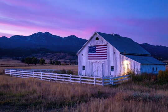 A weathered white barn adorned with the American flag stands proudly against a vibrant twilight sky, framed by rolling hills and distant mountains, evoking a sense of rural Americana.