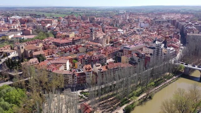 Scenic drone view of modern residential areas of Aranda de Duero city on banks of Duero river on sunny spring day on background of natural rural landscape, Burgos, Spain