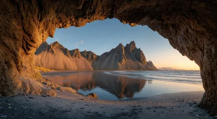 Fototapete Reflection A stunning landscape view of jagged mountains reflected in calm water, framed perfectly by a natural rock archway, bathed in the warm glow of the setting sun.  © Andrew