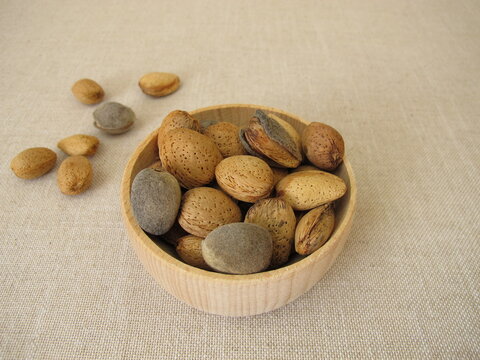 Freshly harvested almonds in a small wooden bowl, some still with their grey‑green fruit hull