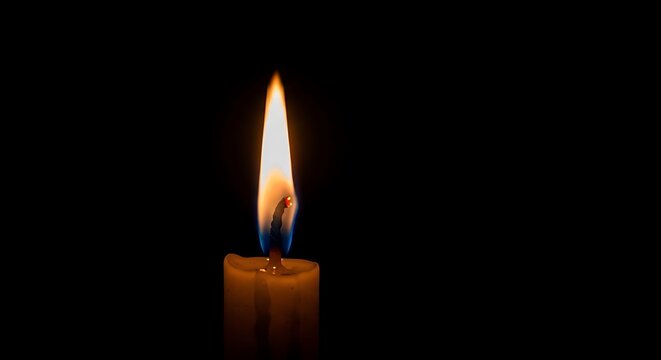 Burning candle flame against a black background representing hope and light
