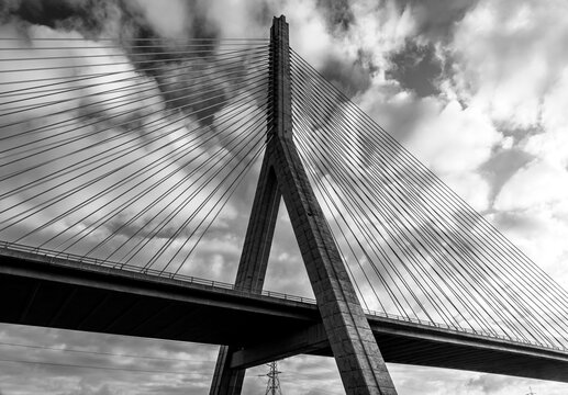 Black and white low-angle view of Flintshire Bridge pylon and stay cables against a dramatic cloudy sky